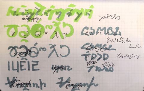 Red notebook page of large painted and pencilled words in several invented scripts